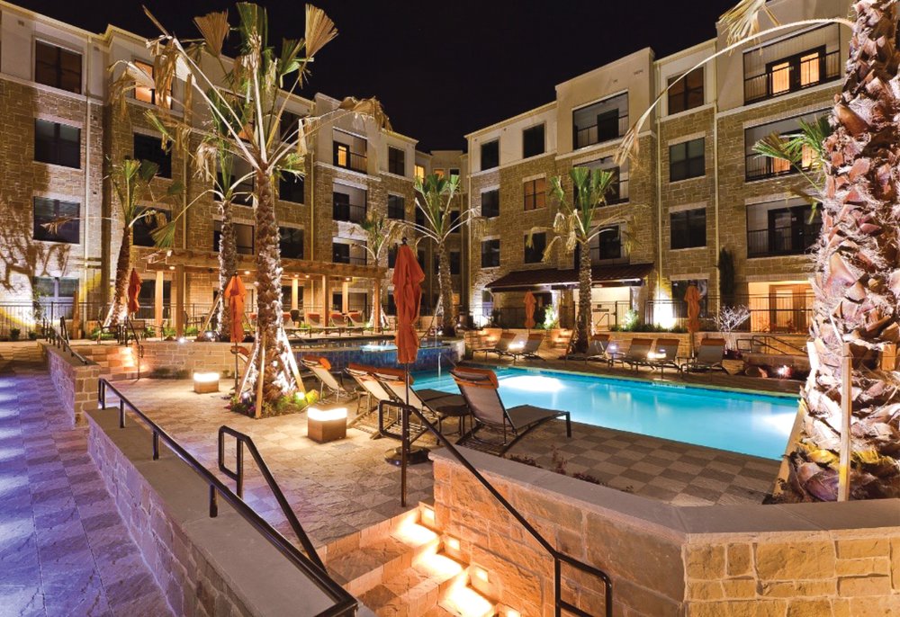 Pool in center of a palm trees which is surrounded by buildings